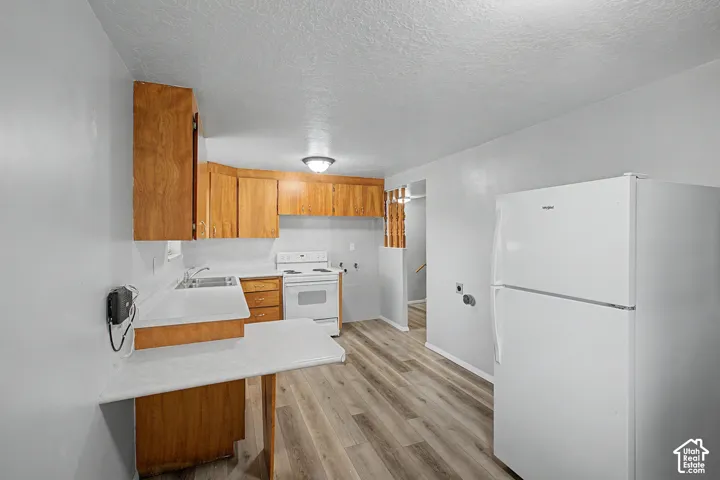 Galley kitchen featuring wood-finish cabinetry, white appliances including a refrigerator and electric range, laminate countertops, and wood-finish flooring throughout