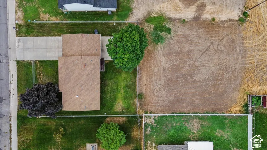 Expansive lot featuring a residential structure with a brown shingle roof, paved driveway, mature trees, and a large undeveloped land area