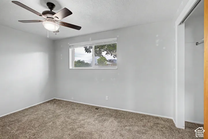 Bright bedroom with neutral carpeting, ceiling fan with integrated lighting, and large casement window providing natural light