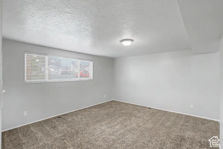Spacious carpeted bedroom featuring neutral wall finishes, abundant natural light from a horizontal window, recessed ceiling lighting, and clean architectural lines throughout