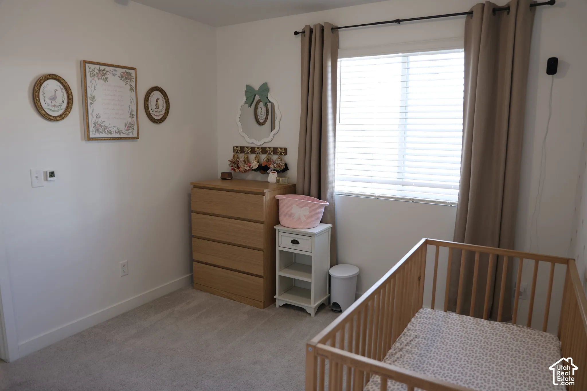 Recessed lighting, light-toned carpeting, wood-finish dresser, window with blinds and drapes, and a wood-finish crib