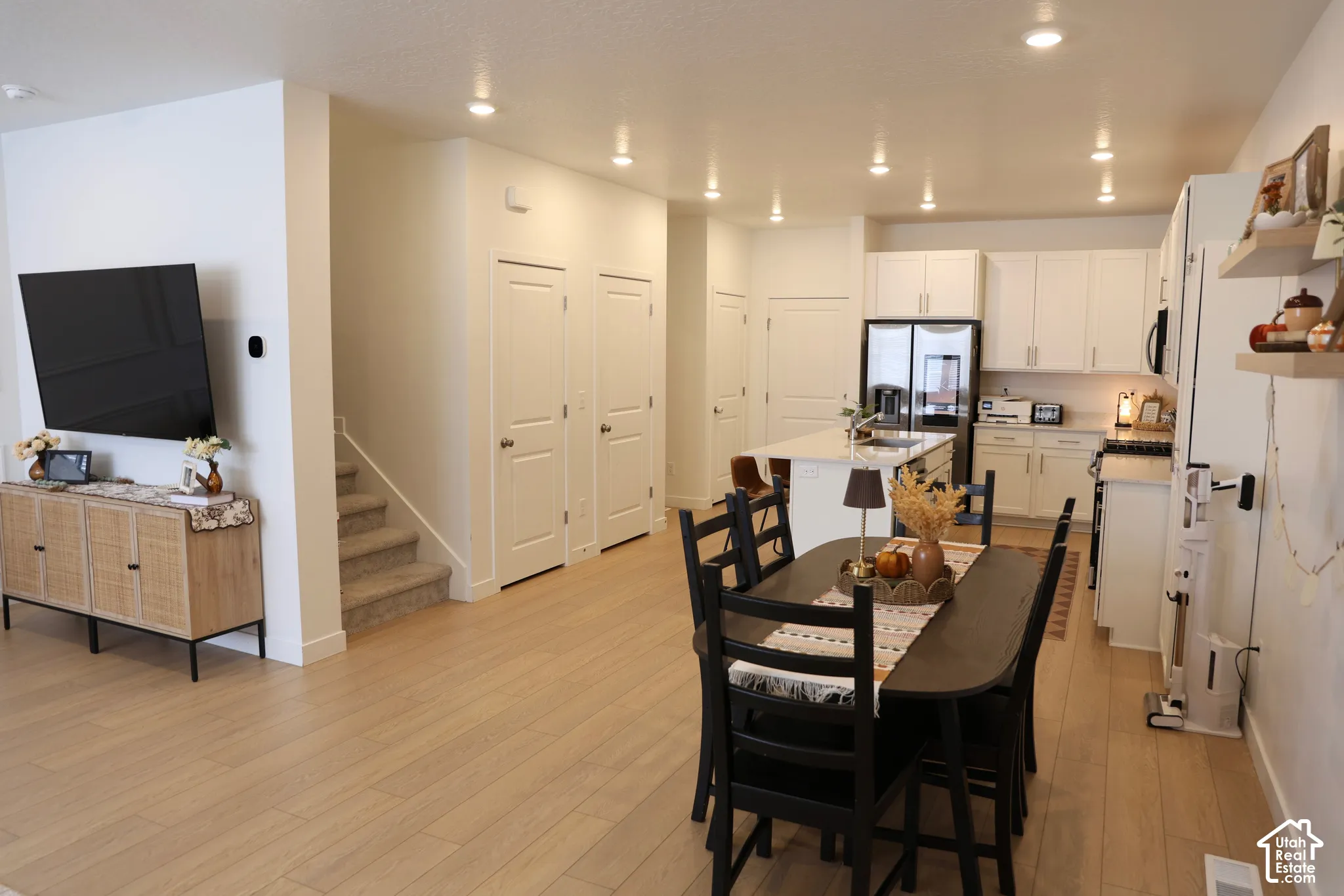 Open-concept living space featuring wood-finish flooring, recessed lighting, a kitchen with white cabinetry, a central island, and a dining area