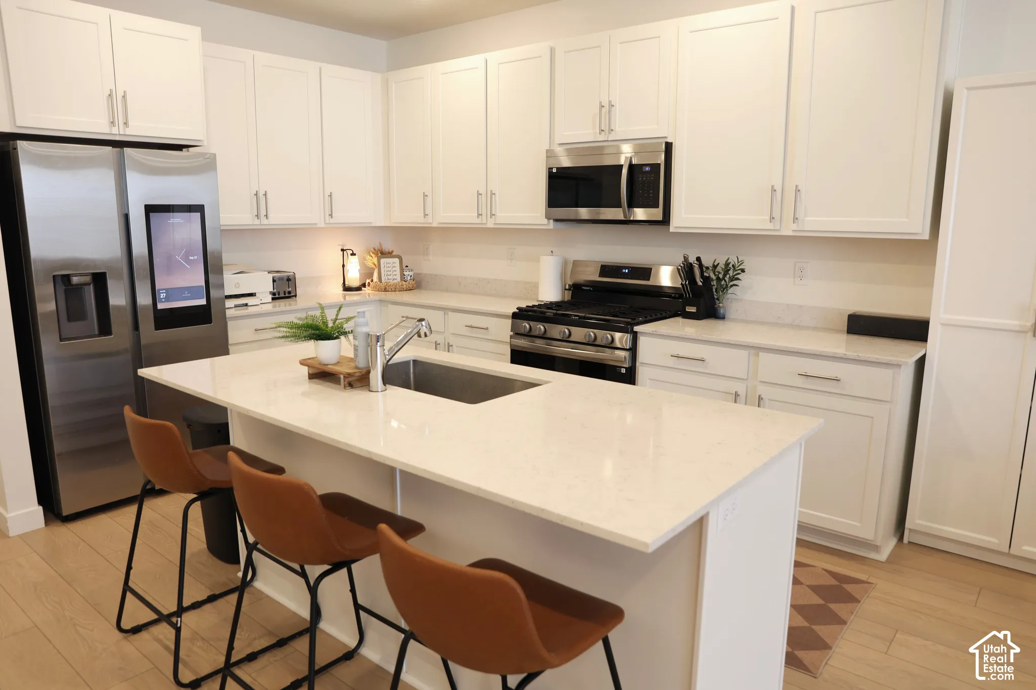 Kitchen featuring a center island with an integrated sink, stainless steel appliances, extensive white cabinetry, light countertops, and wood-finish flooring