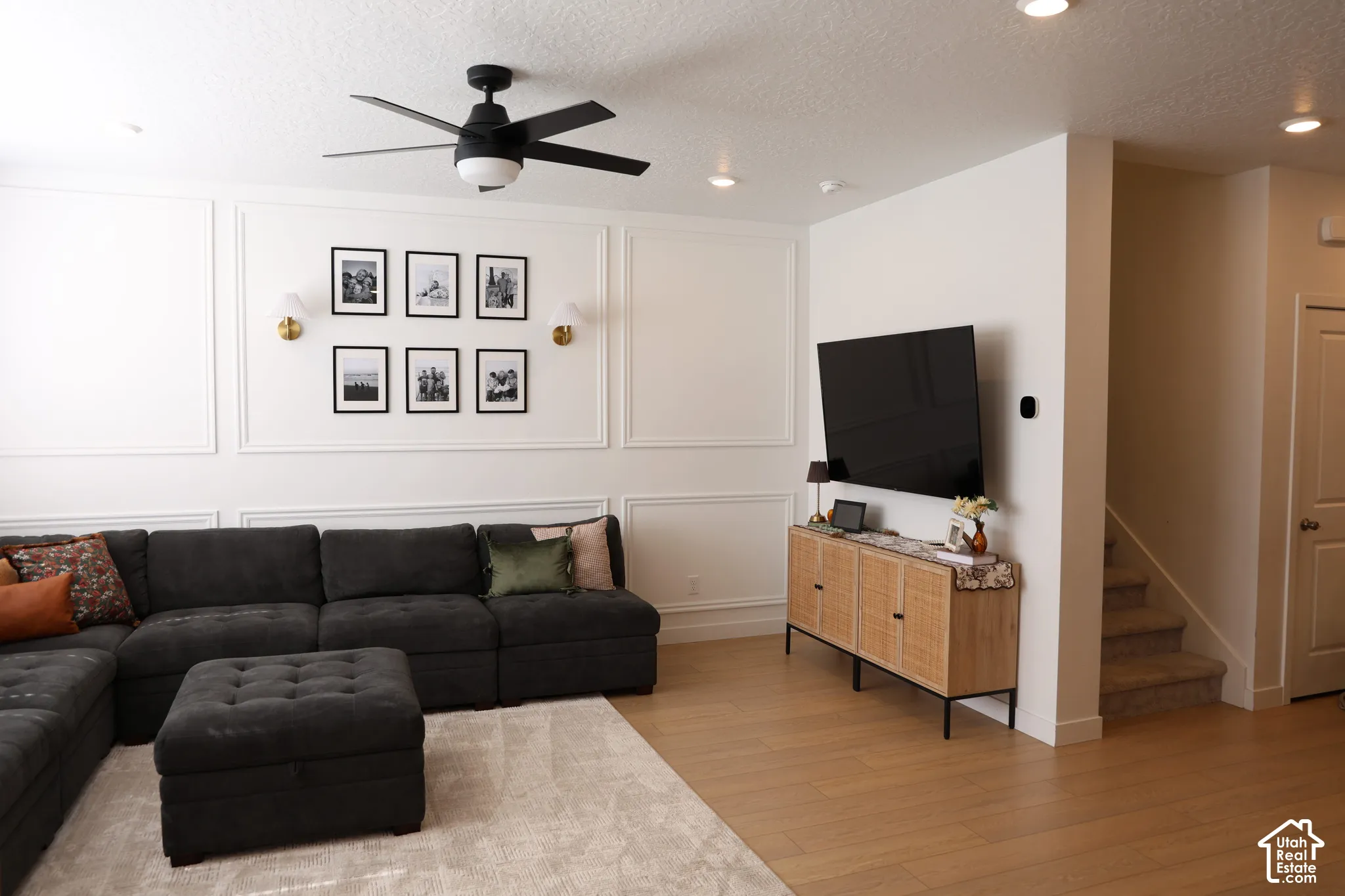 Recessed lighting, wood-finish flooring, accent wall paneling, ceiling fan with integrated lighting, and a carpeted staircase