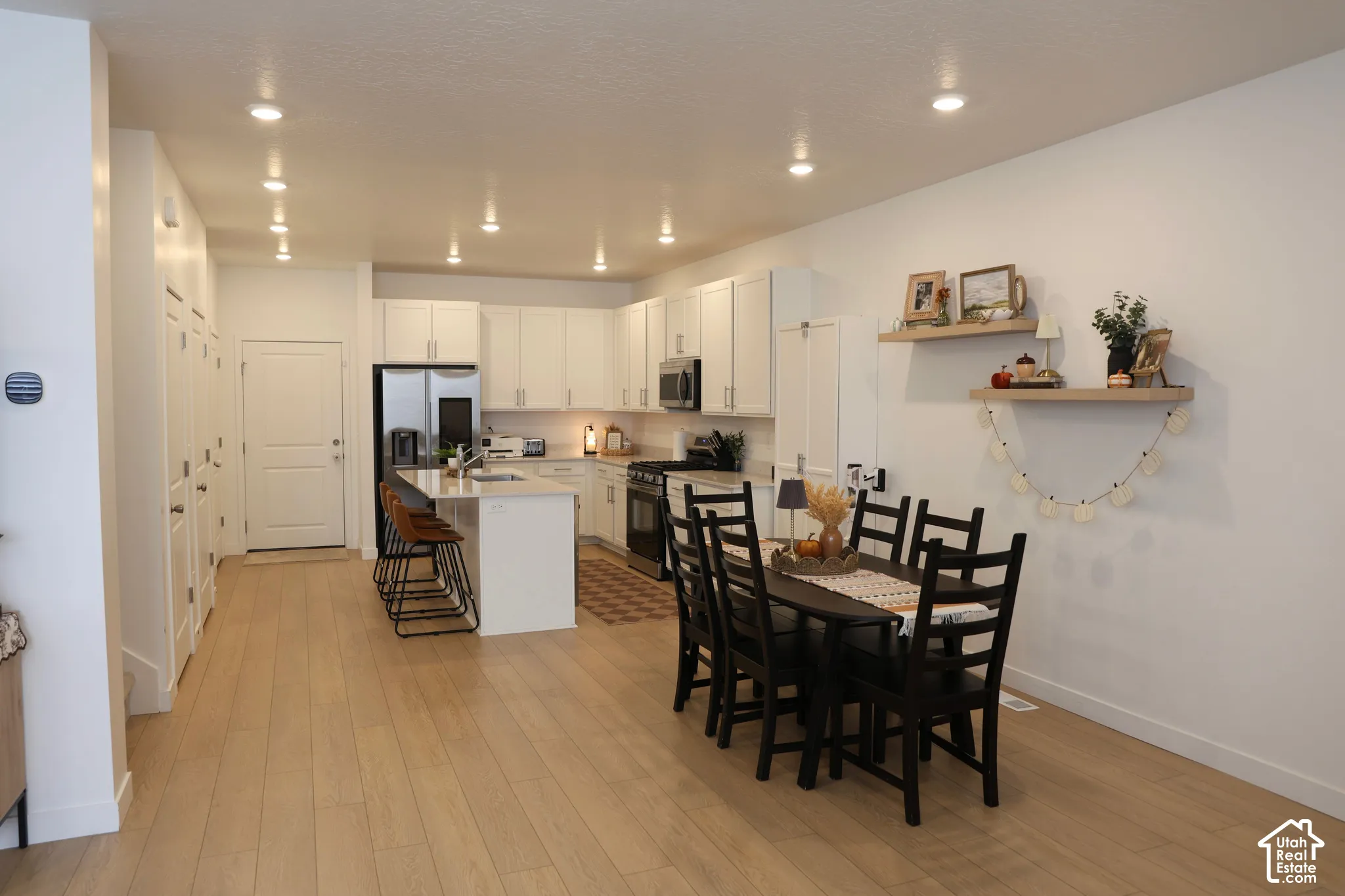Open-concept living area with wood-finish flooring, recessed lighting, white cabinetry, and a kitchen island with seating