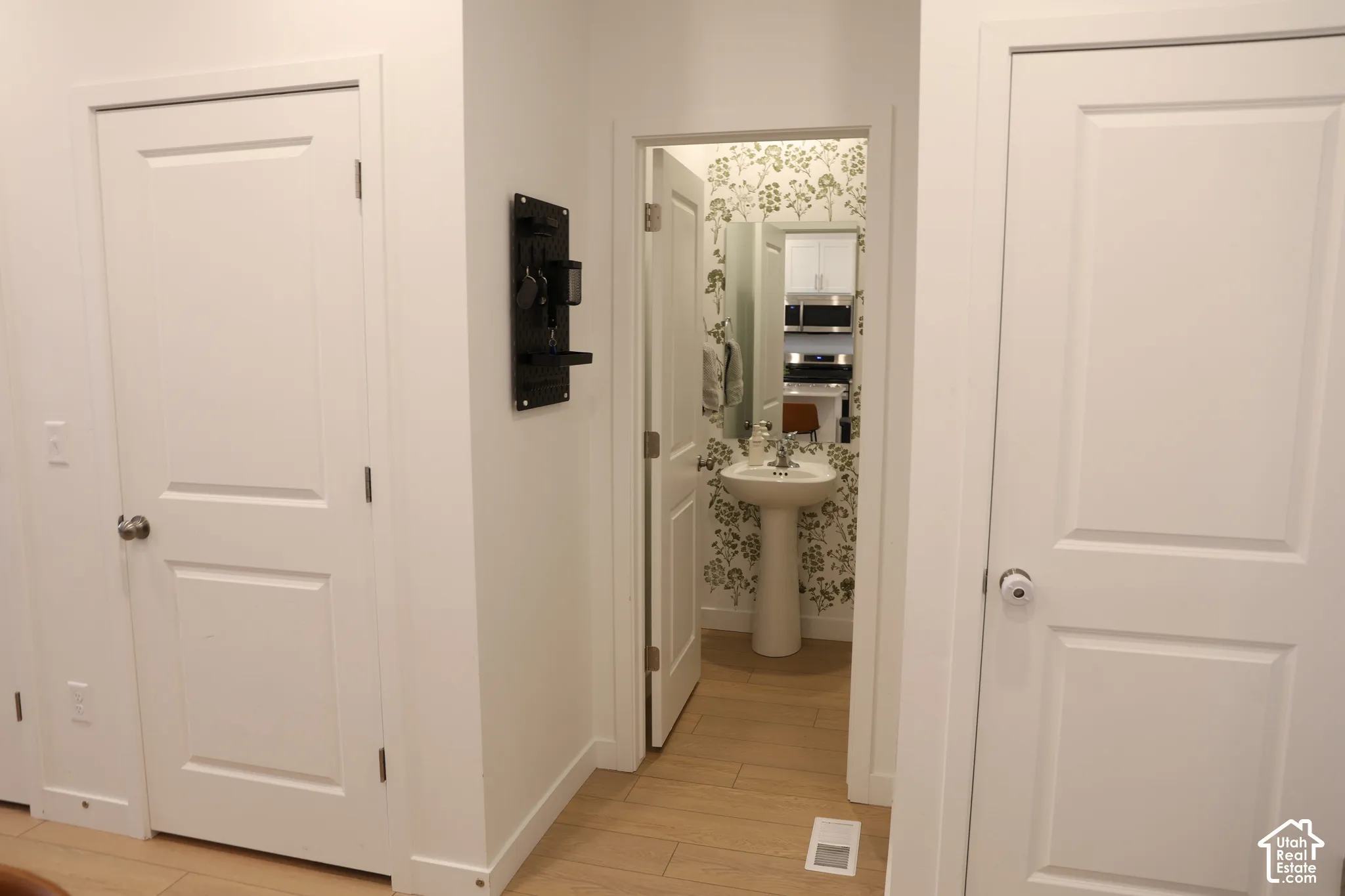 Pedestal sink with chrome faucet, decorative wall covering, and wood-finish flooring