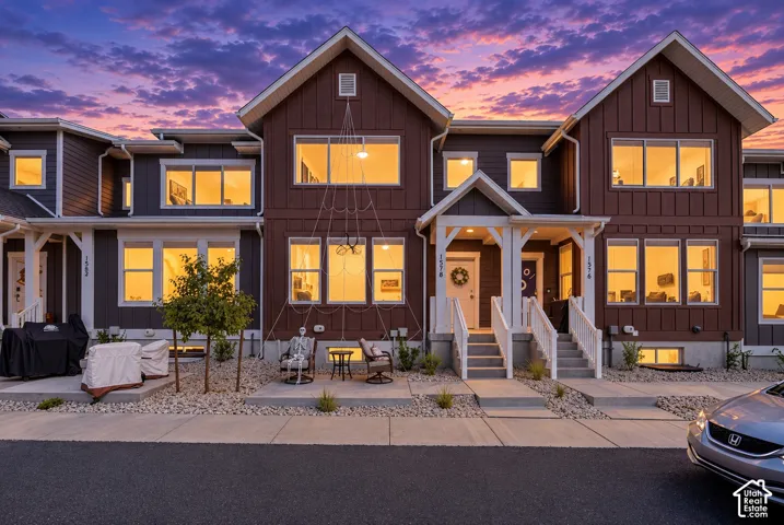 Multi-level townhouse exterior featuring vertical board and batten siding, multiple large windows, and a covered porch entry with white railings