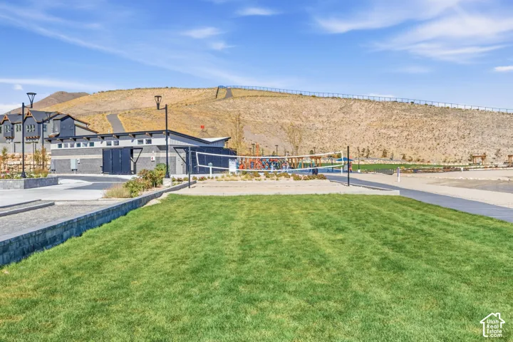 Expansive green space featuring a dedicated sand volleyball court, bocce ball courts, and a contemporary community building with an asphalt parking area