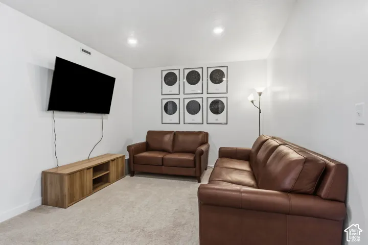 Recessed ceiling lighting, light-colored carpeting, and a wooden media console