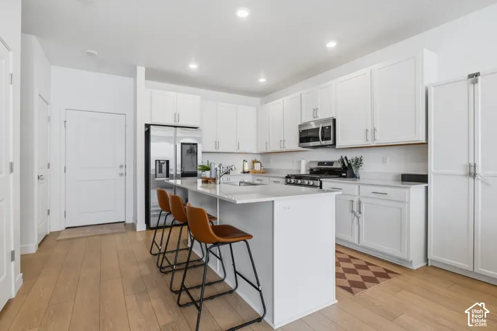 Kitchen with light wood-finish flooring, white cabinetry, stainless steel appliances, a center island with countertop seating, and recessed lighting