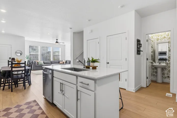 Central kitchen island with an integrated sink and dishwasher, light wood-finish flooring, white cabinetry, and recessed lighting