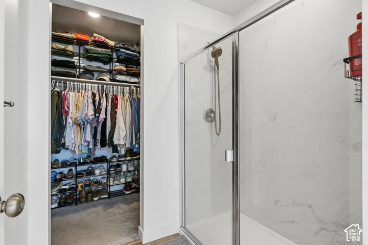 Glass-enclosed shower with a rainfall showerhead, white-veined wall tiles, and an integrated shelf