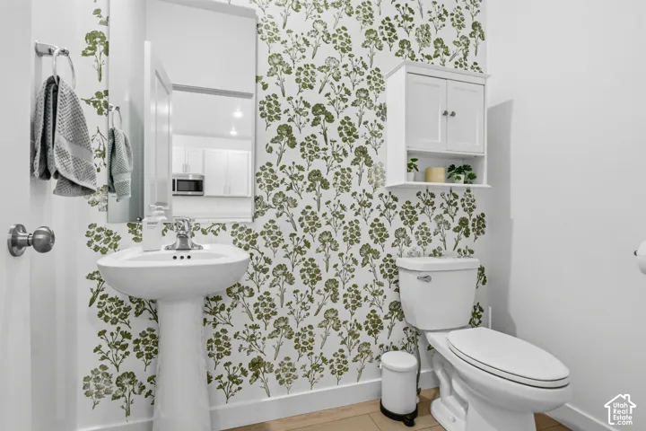 White pedestal sink with chrome faucet, wall-mounted mirror, floral accent wall, white toilet, and wood-finish flooring