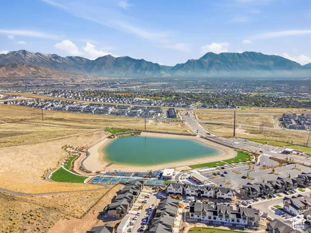 Expansive mountain backdrop, community lake with sandy beach, multiple tennis courts, modern townhomes with dark roofs, and established road infrastructure