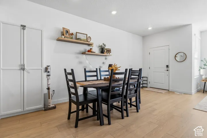 Light wood-finish flooring, white walls, recessed ceiling lighting, built-in white cabinetry, and floating wall shelves