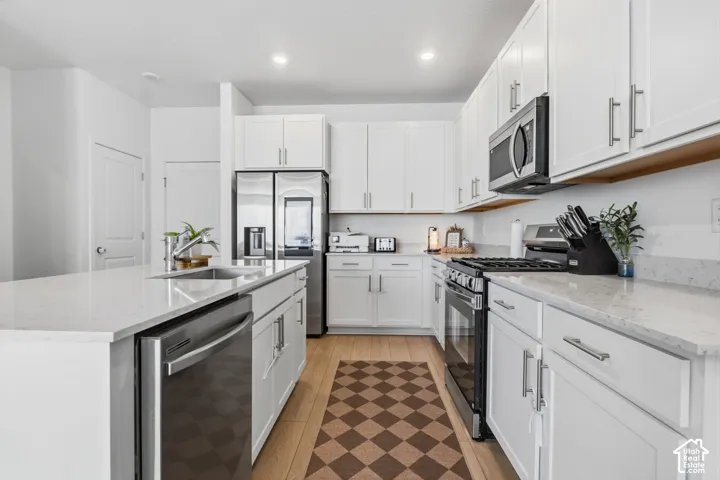 Contemporary kitchen featuring white cabinetry, stainless steel appliances, light-toned countertops, a built-in sink, and wood-finish flooring