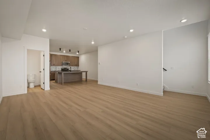 Spacious room featuring wood-finish flooring, recessed lighting, and a kitchen with wood cabinetry and stainless steel appliances