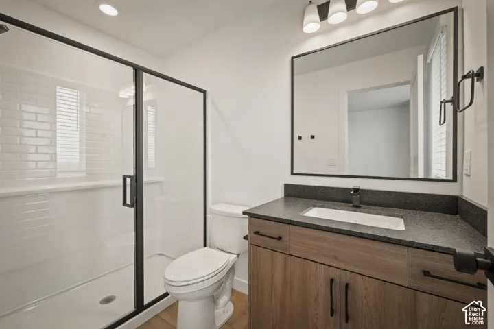Glass-enclosed shower with subway tile surround, wood-finish vanity with dark countertop, rectangular undermount sink, and black fixtures