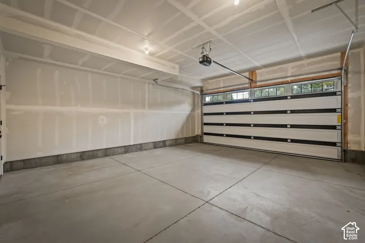Concrete flooring, white walls, overhead lighting, and an automatic garage door with upper window panels