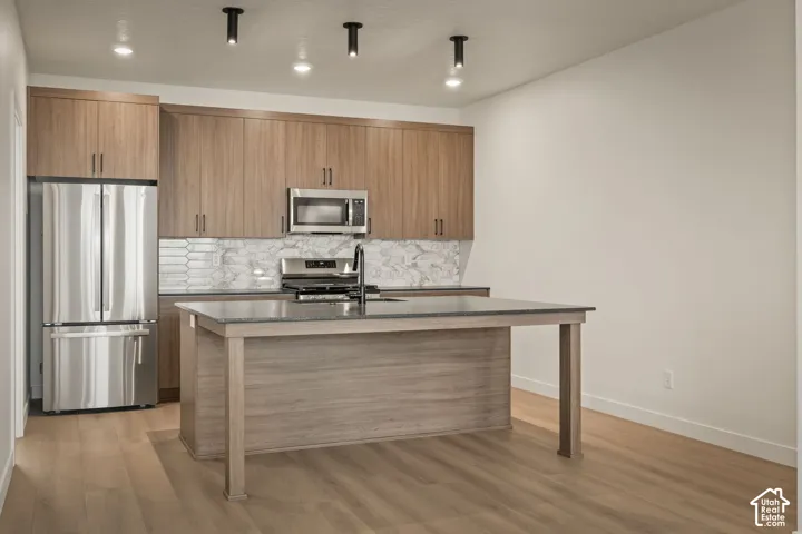 Kitchen featuring wood-finish cabinetry, stainless steel appliances, a center island with a dark countertop, and wood-finish flooring