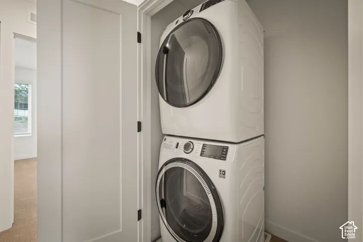 Stackable washer and dryer appliances within a dedicated recess, featuring a solid white door with dark hardware
