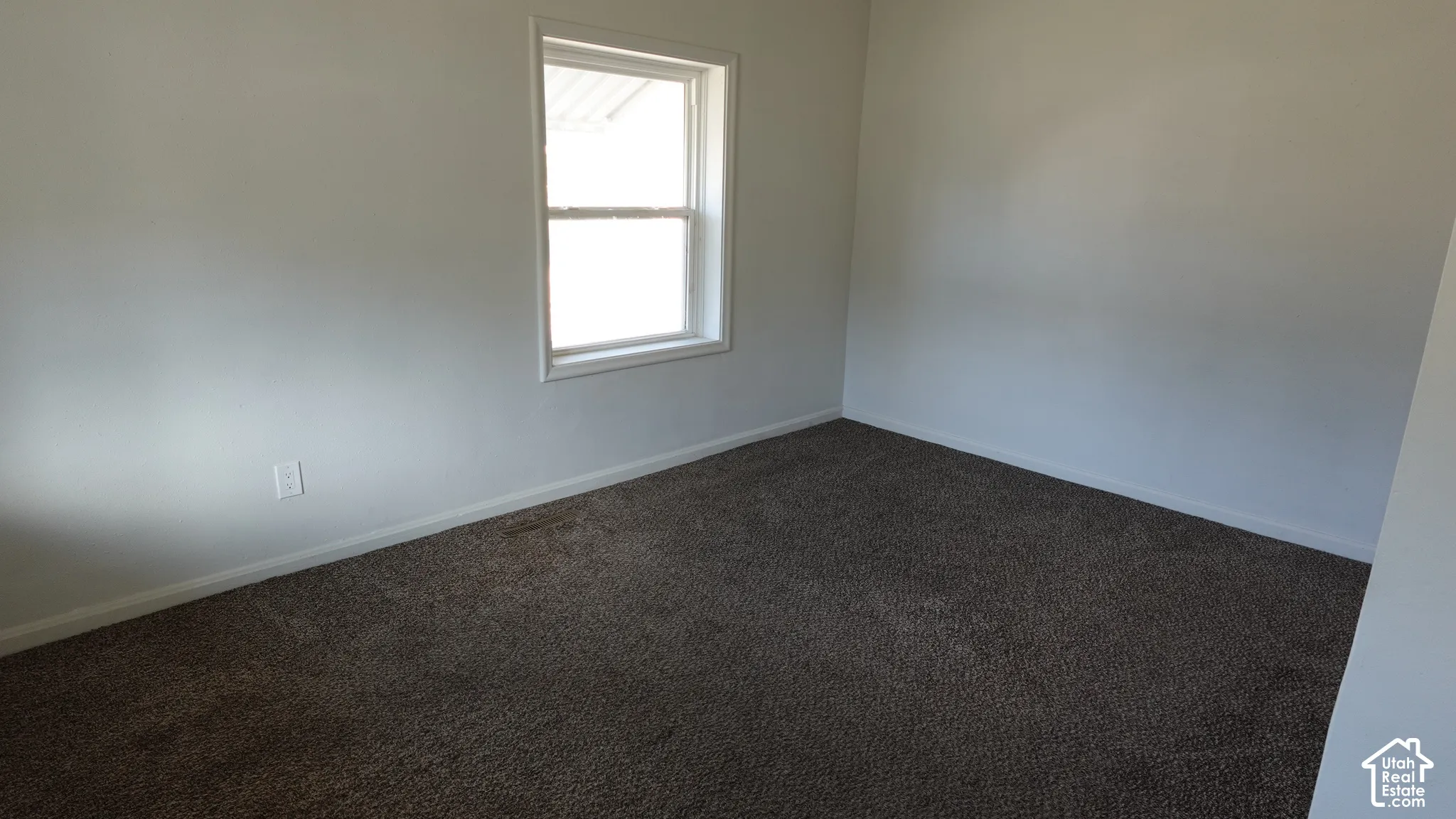Neutral wall tones, window with white trim, and dark carpeting