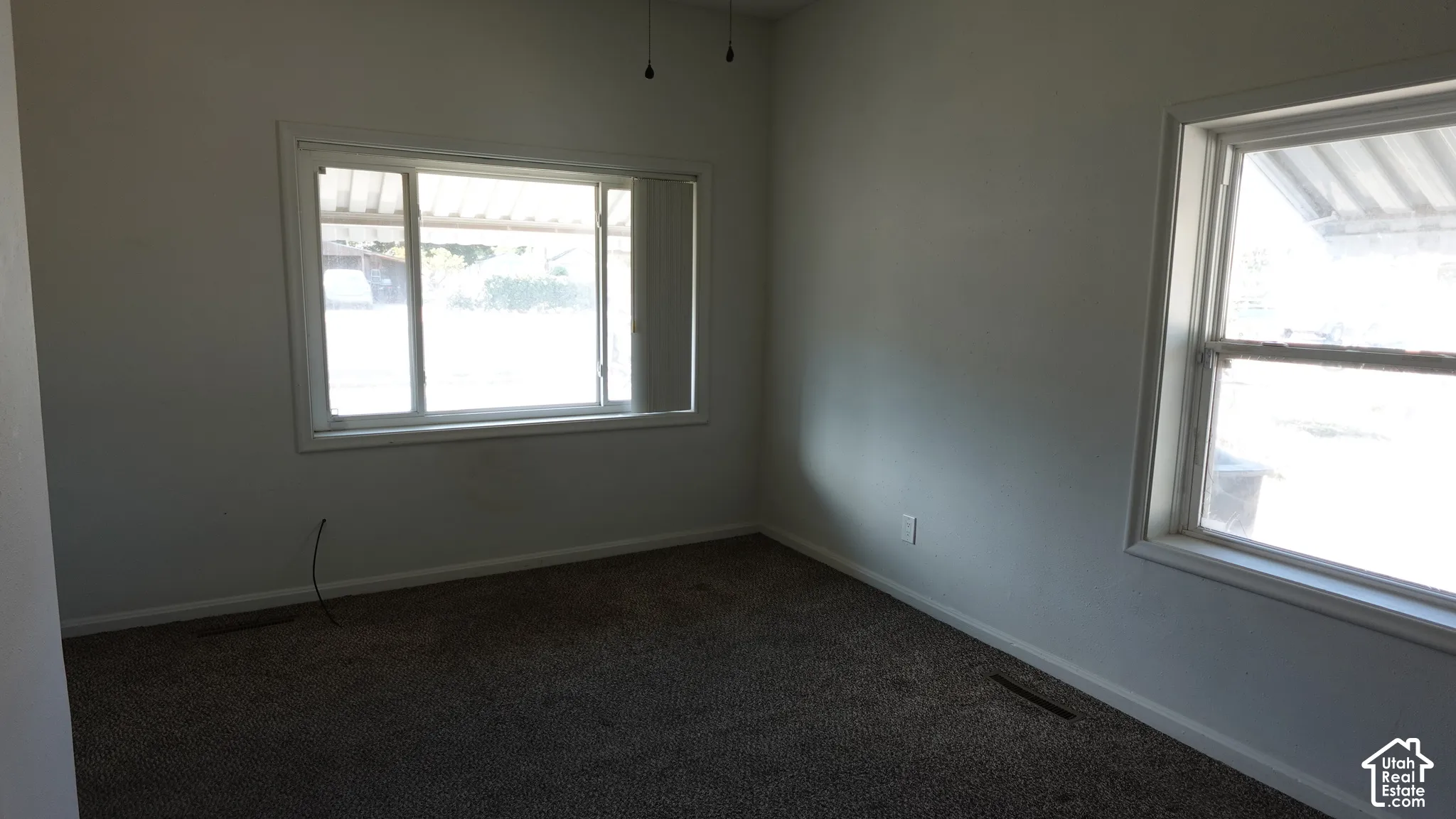 Neutral wall color, carpet flooring, two windows with white trim, and a ceiling fan