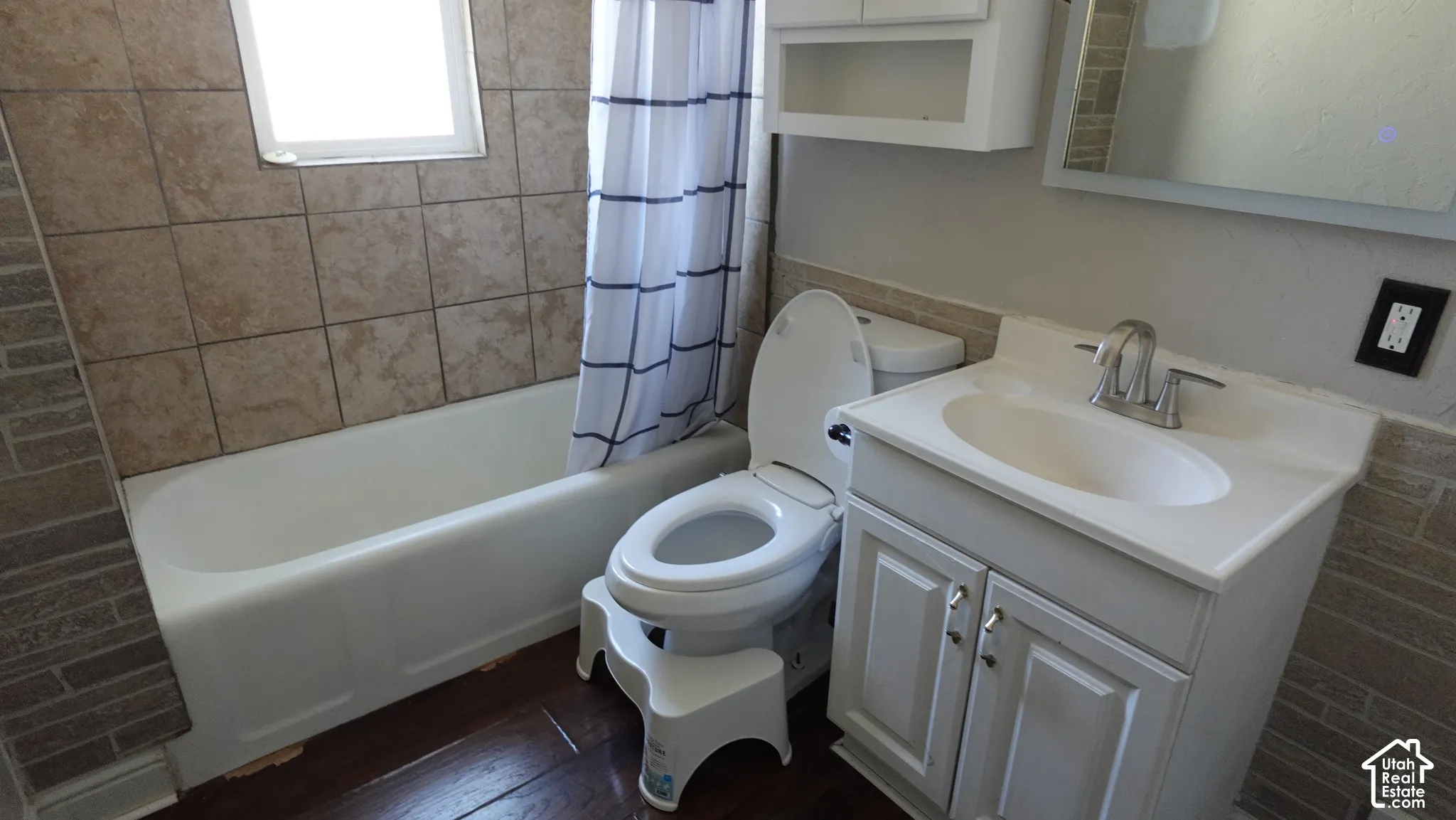 Bathtub with tiled surround, white vanity with integrated sink, and wood-finish flooring