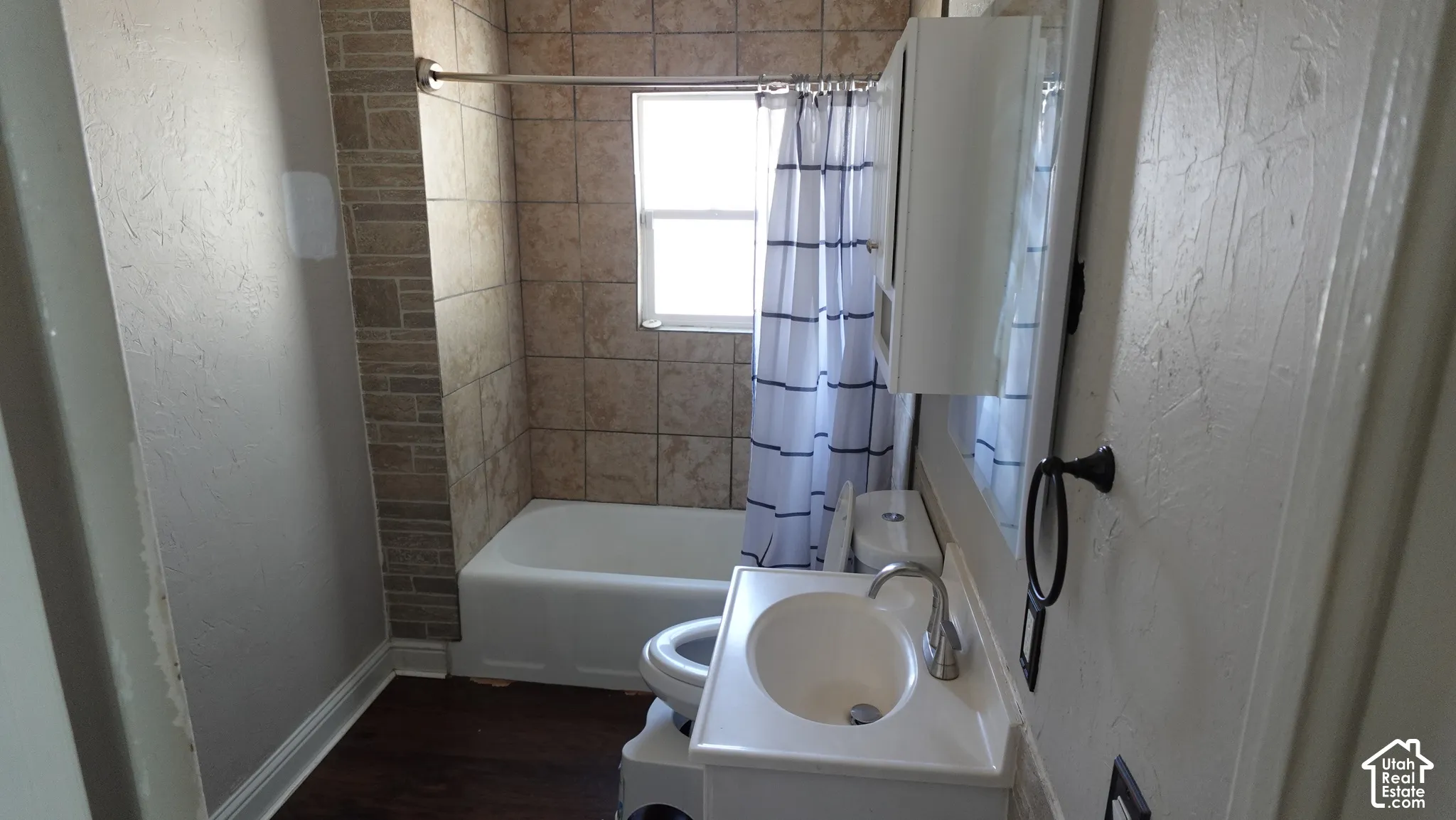 Ceramic tile shower surround with integrated window, white bathtub, wood-finish flooring, white vanity with integrated sink, and wall-mounted medicine cabinet