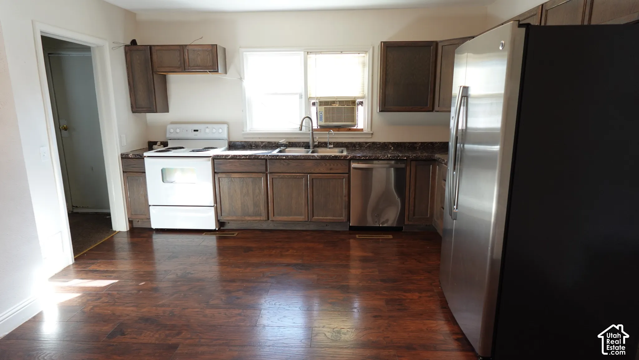 Spacious kitchen featuring rich wood-finish cabinetry, stainless steel appliances including refrigerator and range, and a large center island with sink