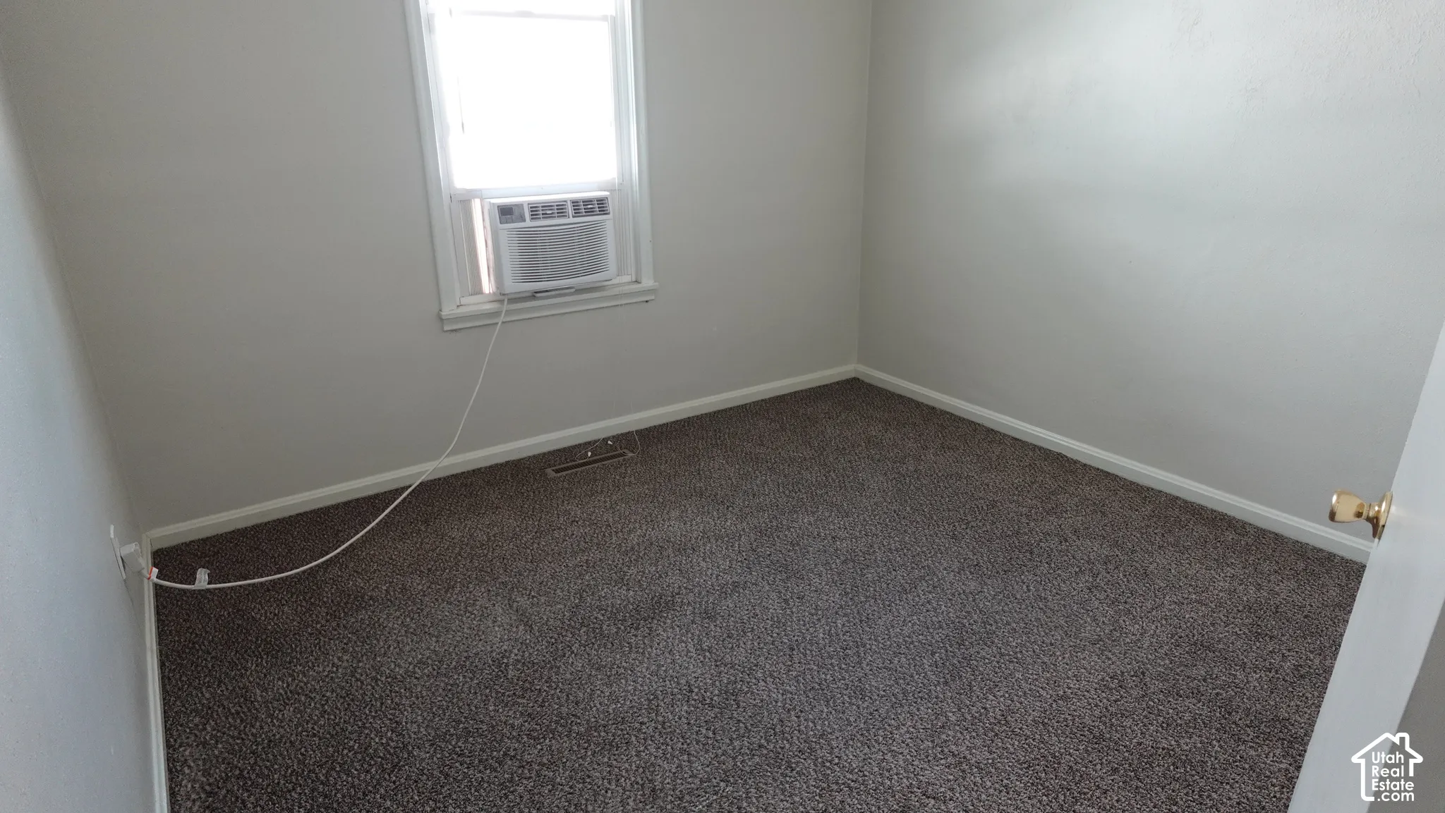 Spacious bedroom featuring neutral wall finishes, carpeted flooring, and abundant natural light from a window with integrated air conditioning unit