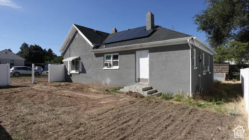 Gray stucco exterior with a dark shingle roof, solar panels, and white window trim