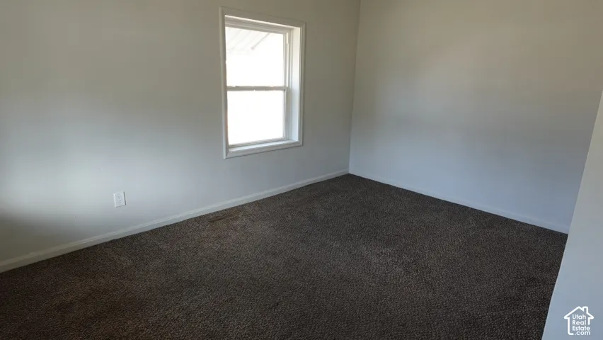 Neutral wall tones, window with white trim, and dark carpeting