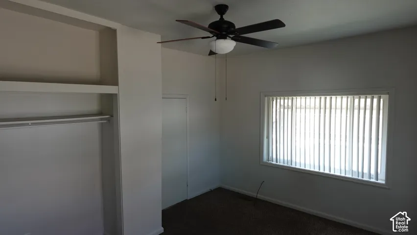 Bright secondary bedroom featuring large vertical blinds, ceiling fan with integrated lighting, and dark flooring throughout