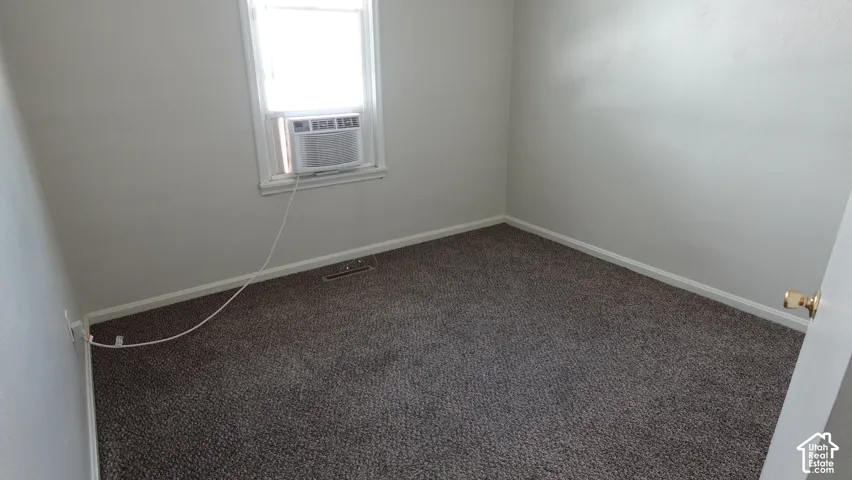 Spacious bedroom featuring neutral wall finishes, carpeted flooring, and abundant natural light from a window with integrated air conditioning unit