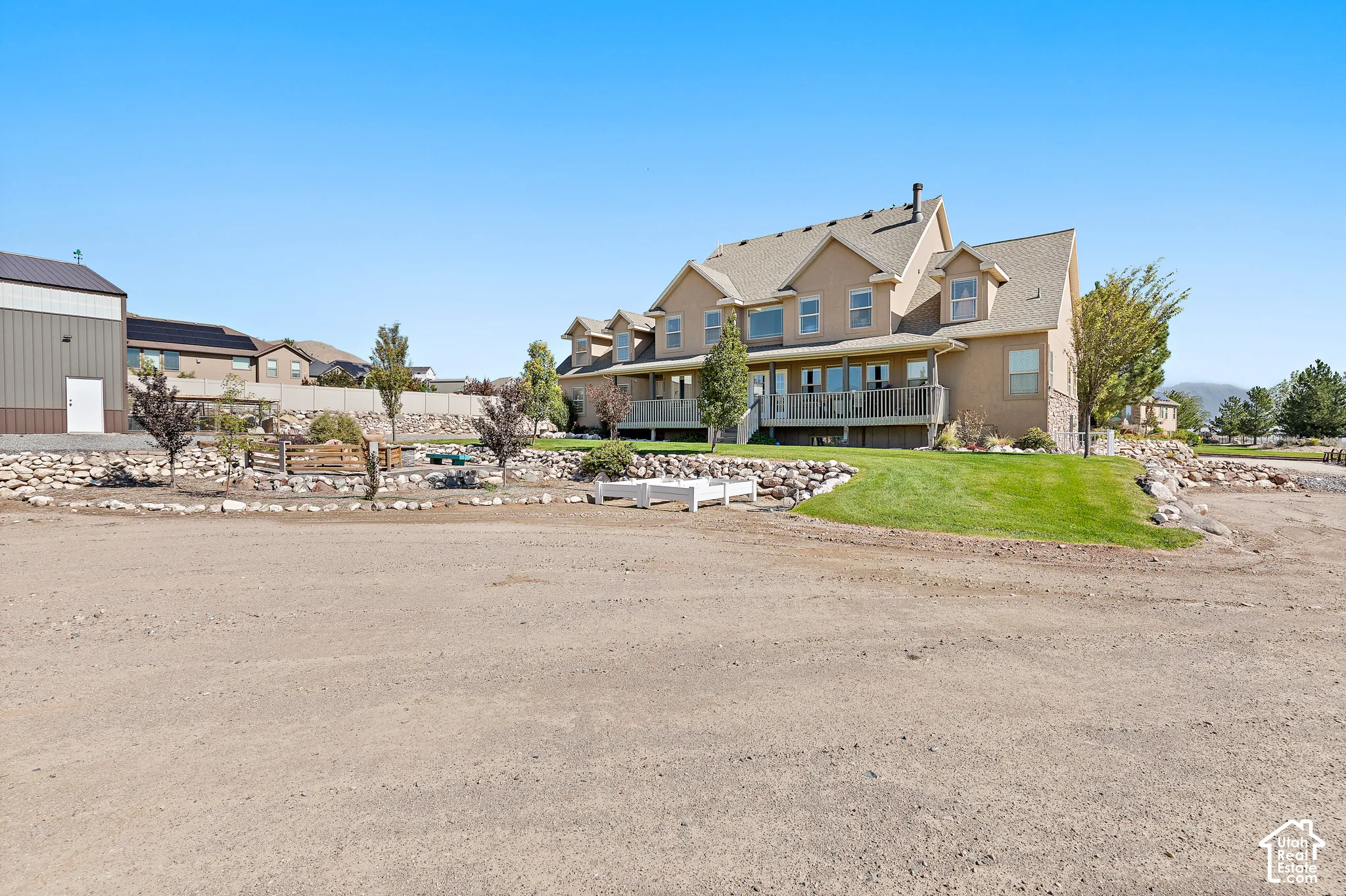 Multi-story exterior with dormer windows, covered deck, and an extensive lawn with rock landscaping