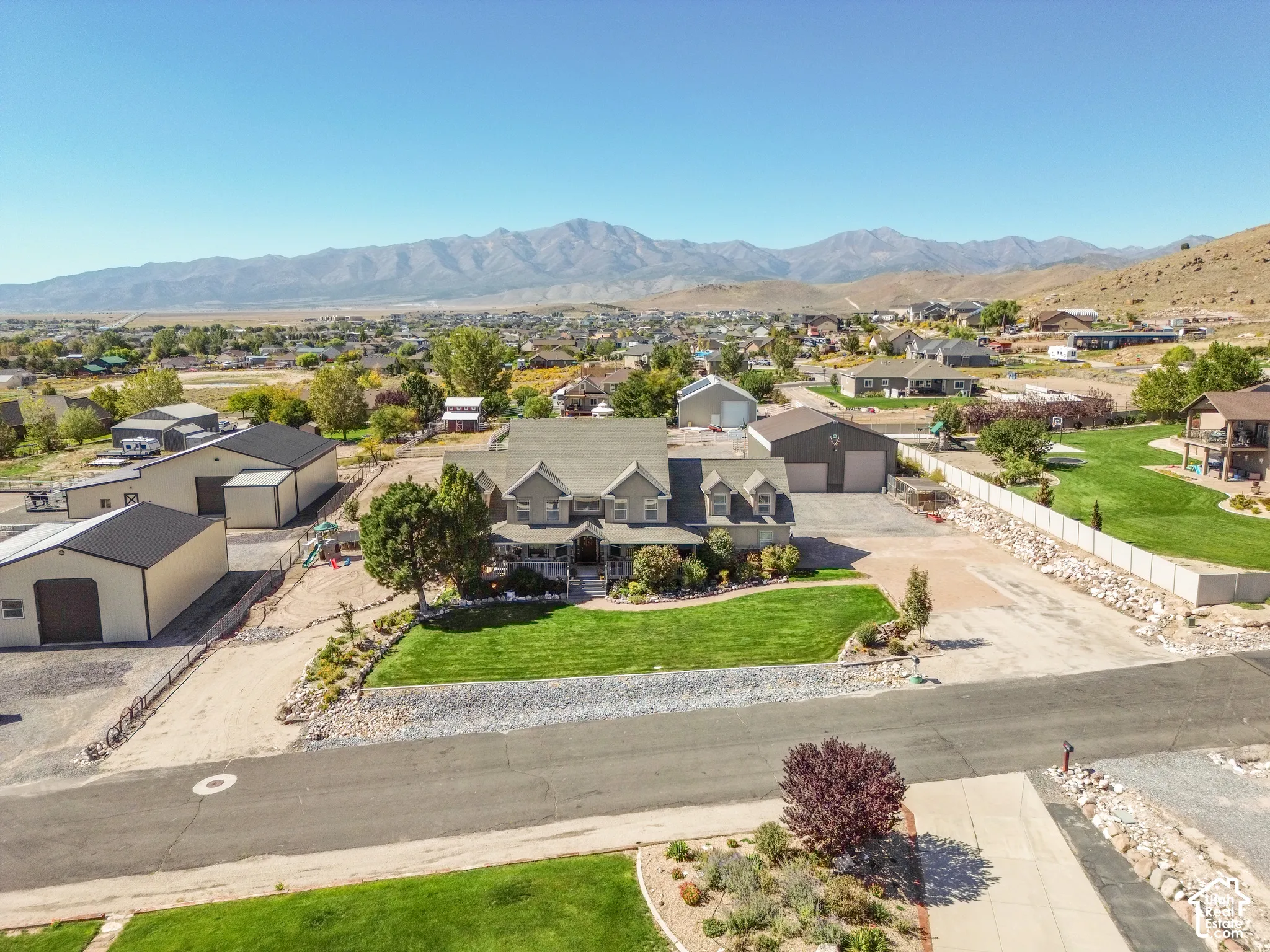 Expansive property featuring a substantial residence, multiple detached garages, manicured lawn, and a broad paved driveway