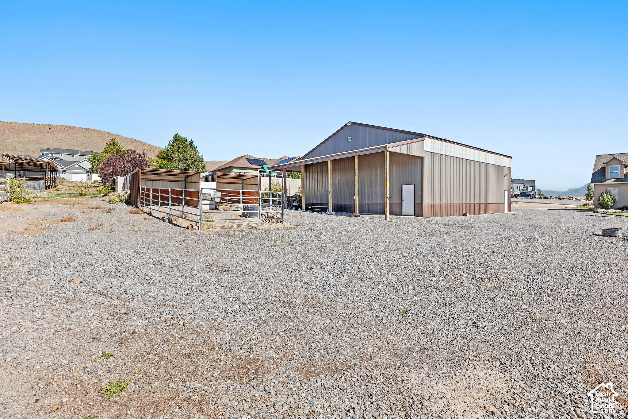 Large gravel lot with a steel-sided auxiliary building featuring an open-front covered area and a separate entry door