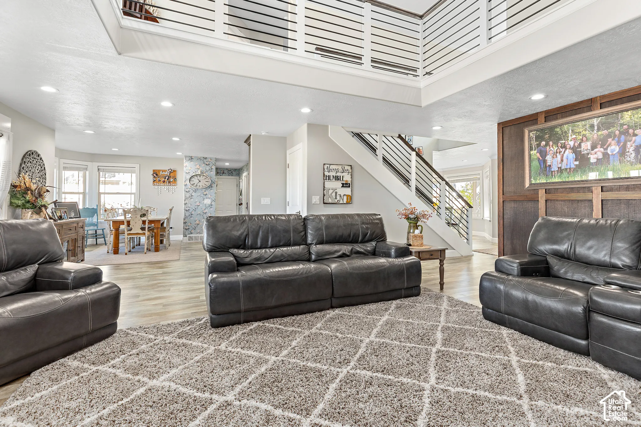 Spacious living area featuring high ceilings, wood-finish flooring, and a modern open-tread staircase with horizontal railings