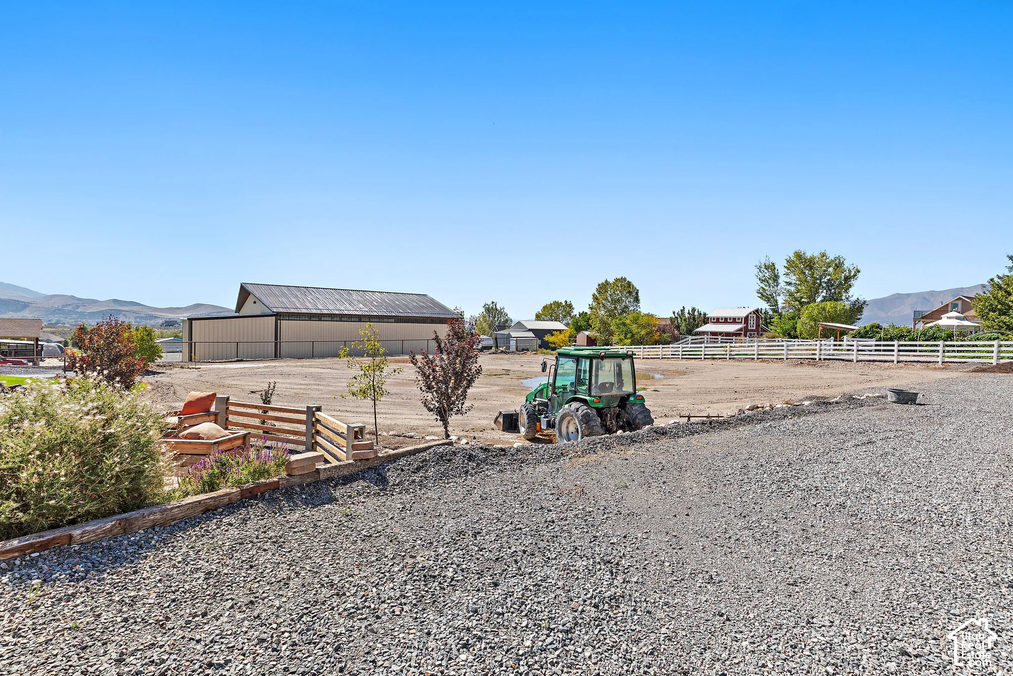 Expansive gravel surface, white fencing, and a large metal-clad barn structure