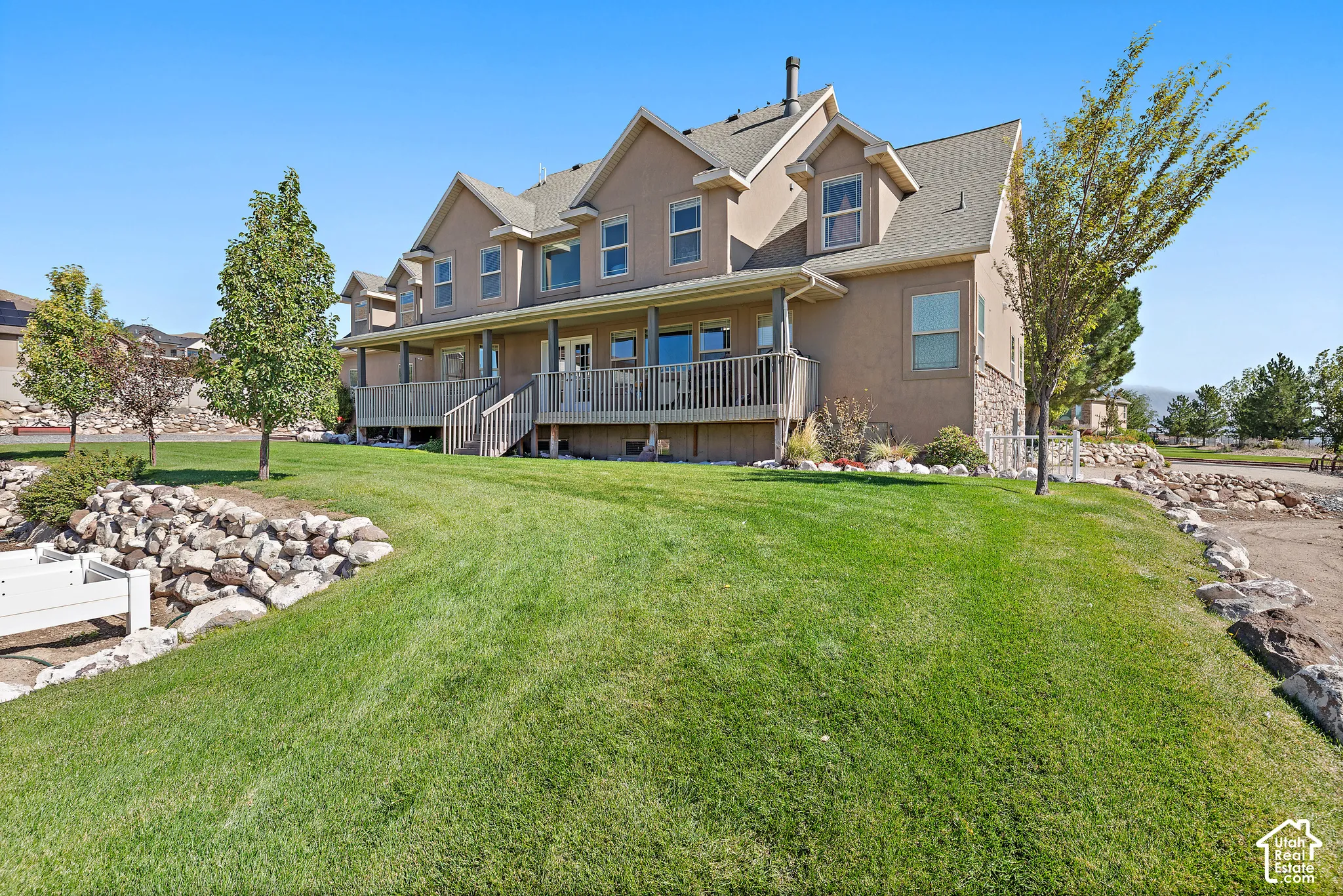 Expansive rear exterior featuring multiple dormer windows, a full-length wooden deck, and a stone retaining wall