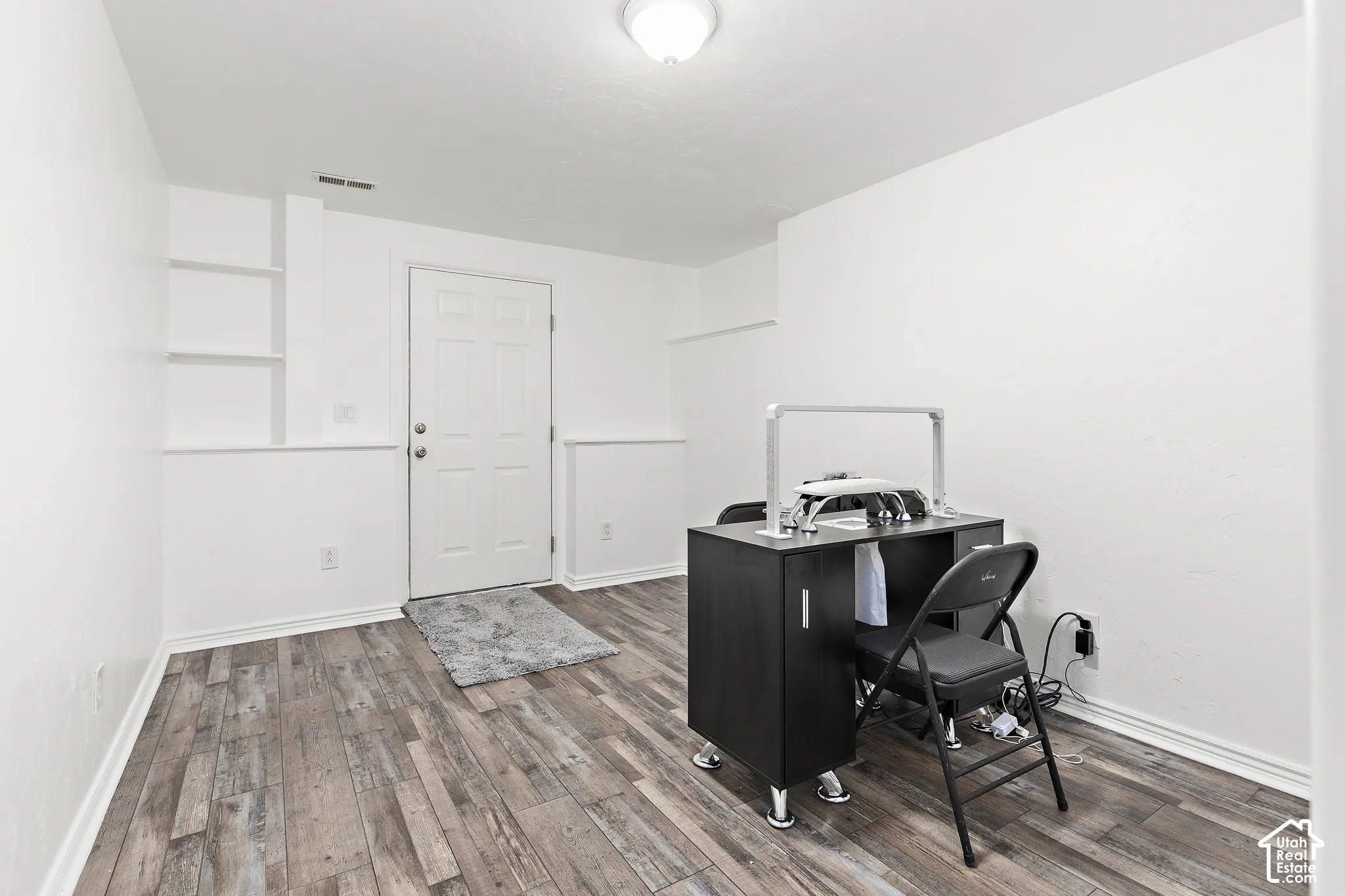 Wood-finish flooring, white paneled walls, built-in shelving, white door with textured glass detail, and overhead dome lighting