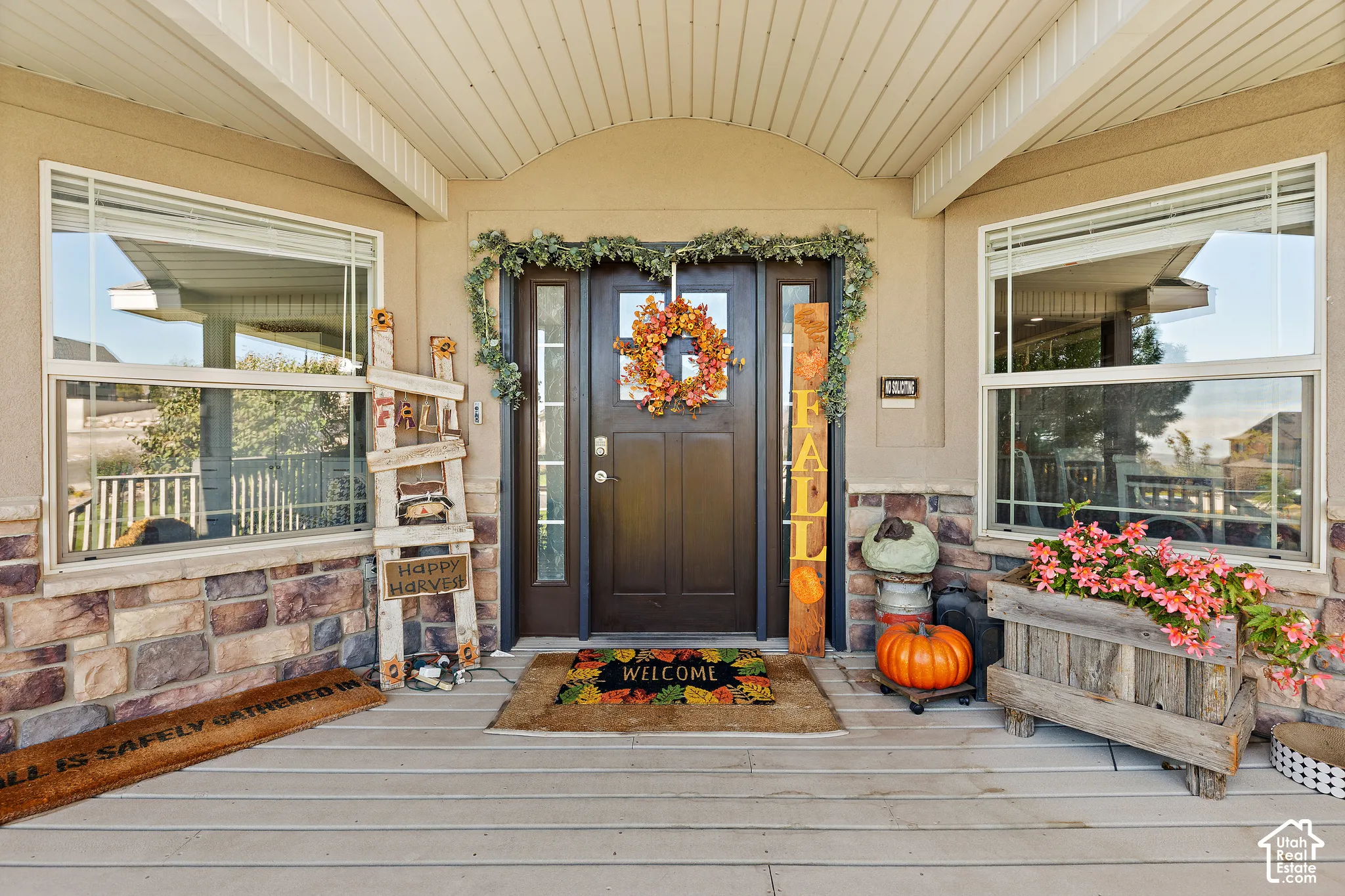 Front entry with a dark-stained door and sidelights, flanked by large windows, stone facade accents, and a covered porch with a light-colored ceiling