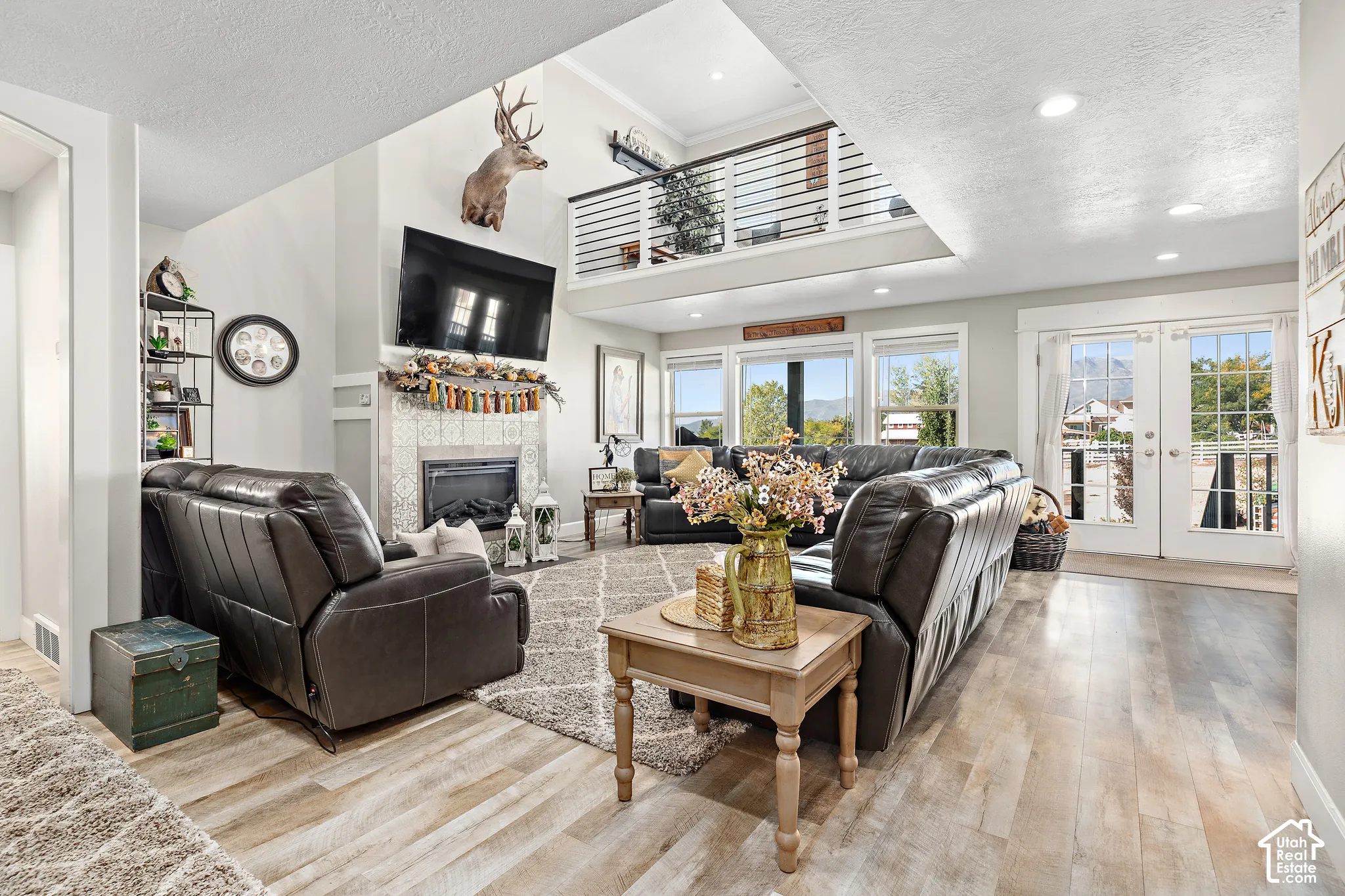 Vaulted ceiling, open mezzanine with metal railing, wood-finish flooring, fireplace with tile surround, and French doors