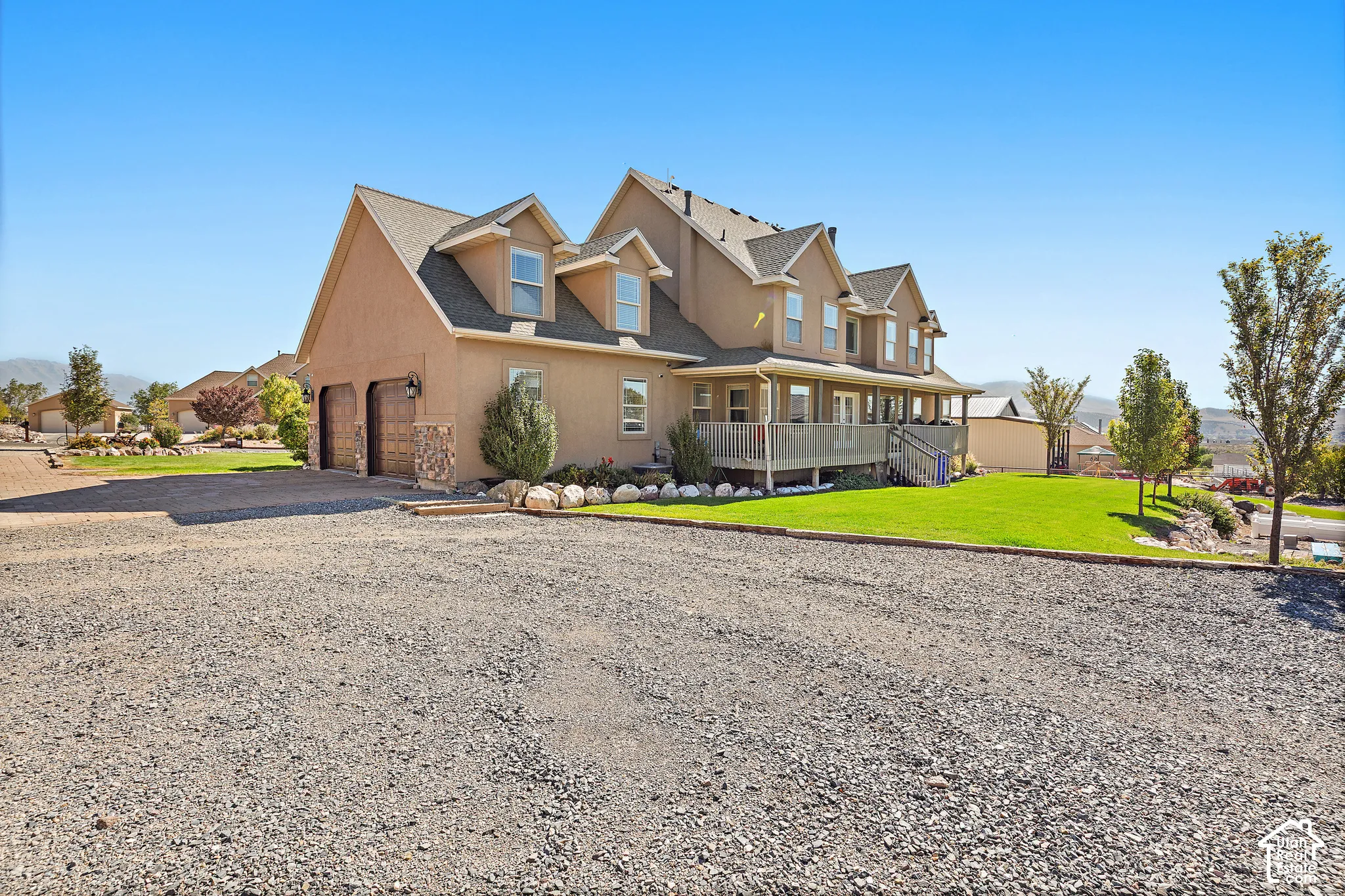 Stucco exterior residence with dormer windows, a covered porch, an attached garage with wood-paneled doors, and a manicured lawn