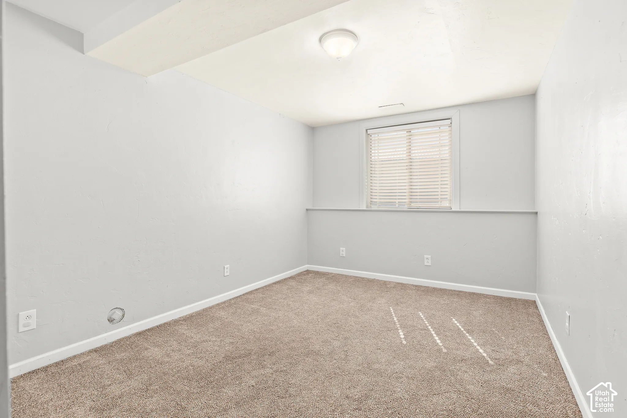 Carpeted flooring, recessed window with blinds, ceiling-mounted light fixture, and light-toned wall paint