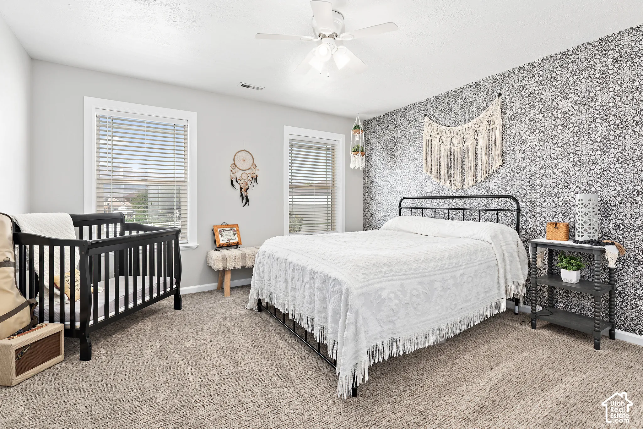 Textured carpet flooring, ceiling fan, multiple windows with blinds, accent wall with patterned wallpaper