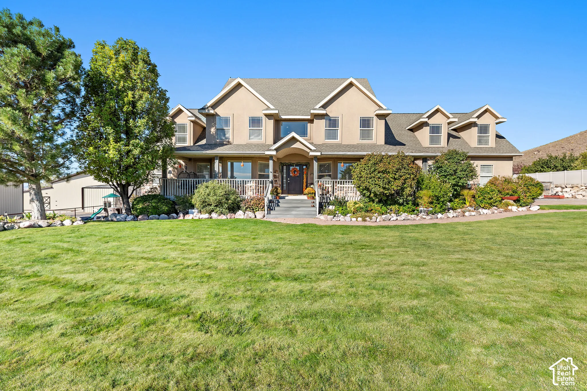 Stucco exterior with multiple gables and dormer windows, featuring a covered front porch and a spacious lawn