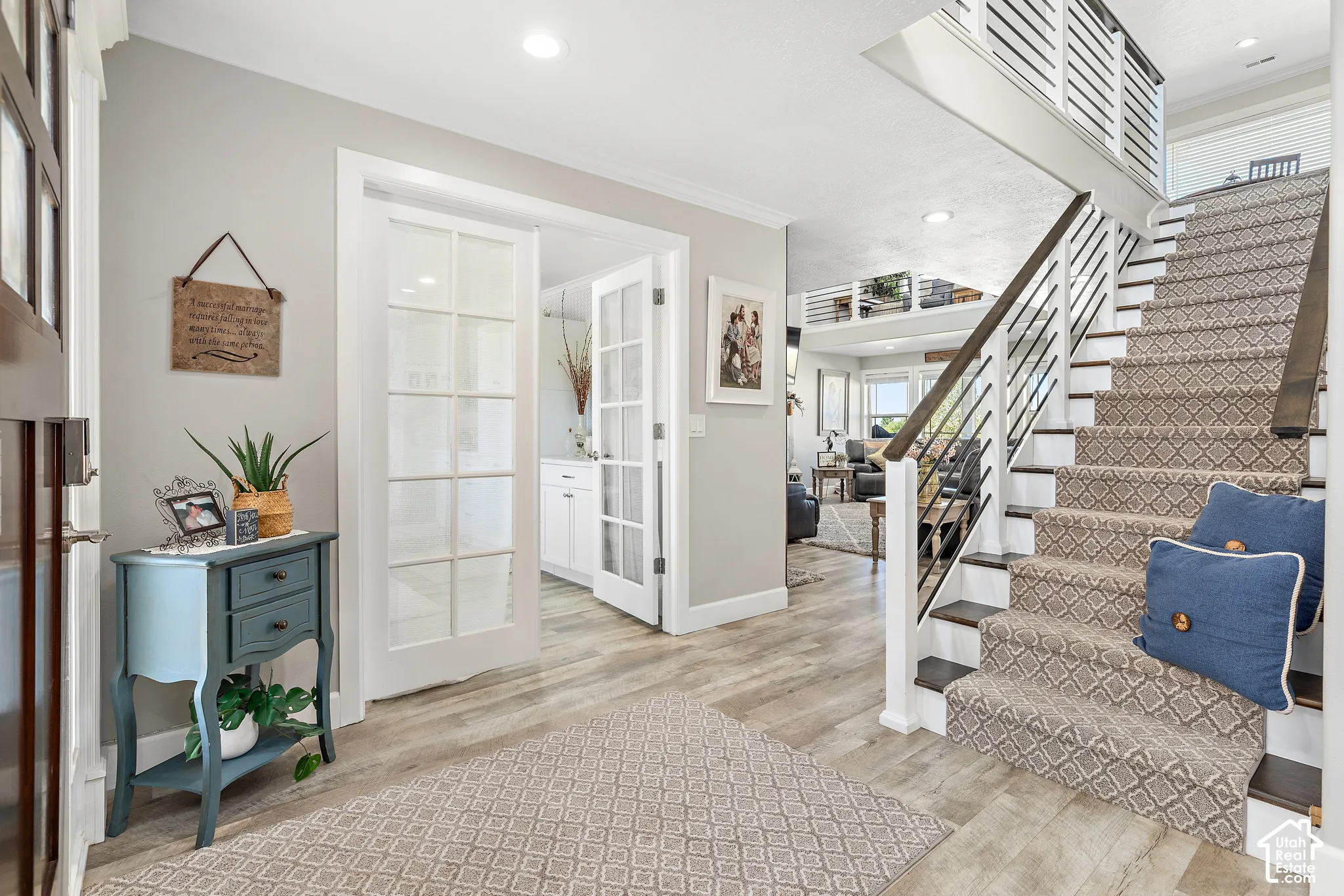 Two-story entry featuring wood-finish flooring, a carpeted staircase with dark wood treads, and white newel posts with dark metal balusters