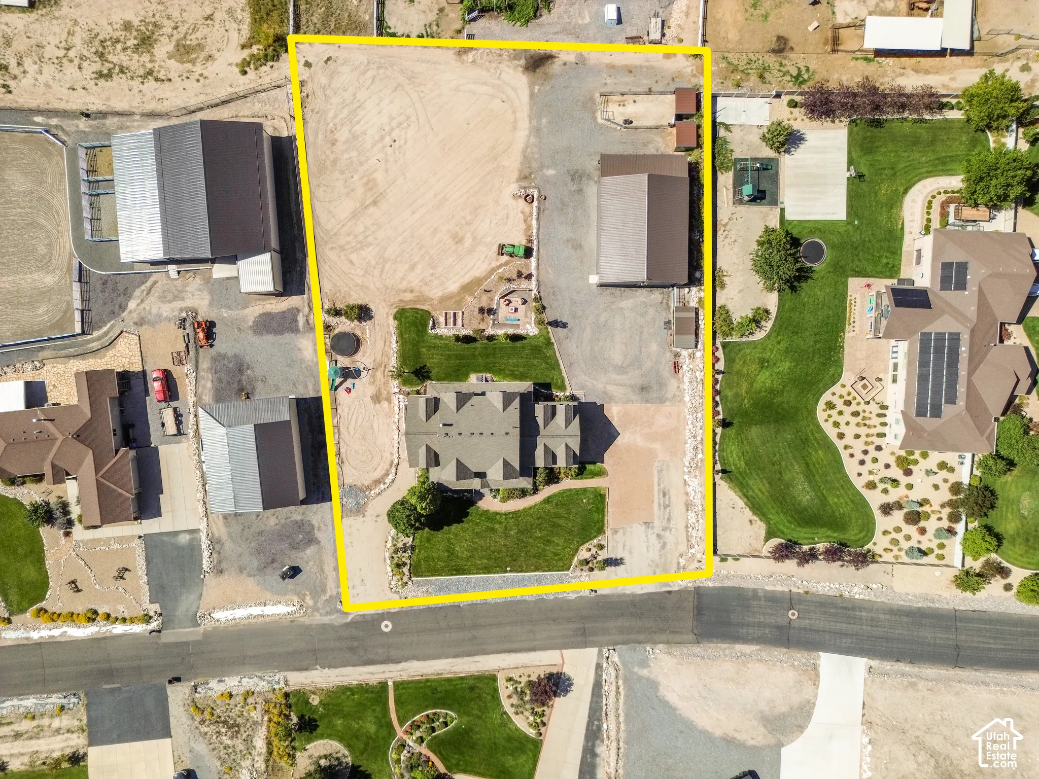 Aerial property overview featuring a main residence, two outbuildings, extensive unpaved areas, and established landscaping